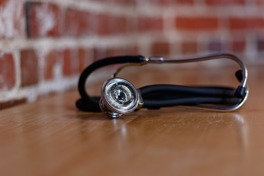 Stethoscope resting on a wooden desk in front of a brick wall