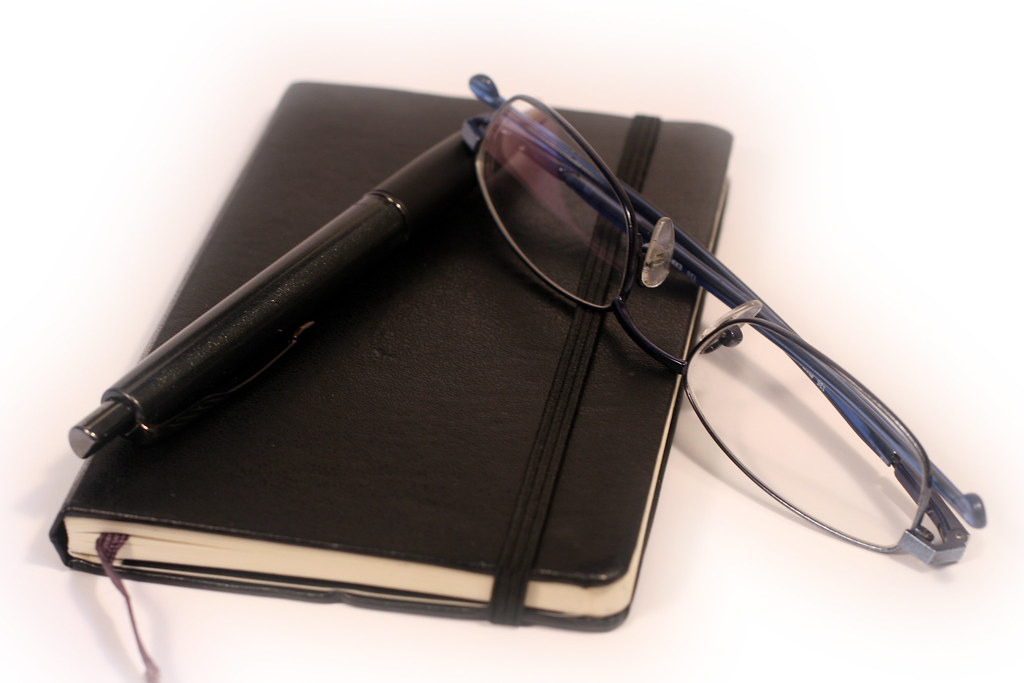 Black notebook planner with a pen and reading glasses
